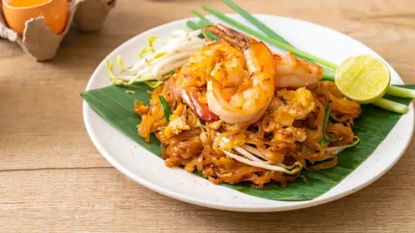 Pad Thai con camarones, perfecto para tu curso de cocina tailandesa. Servido sobre hoja de plátano, con brotes de soja, cebolleta y limón.