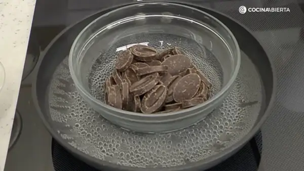 Chocolate troceado derritiéndose suavemente en un bol de cristal sobre un baño maría hirviendo.