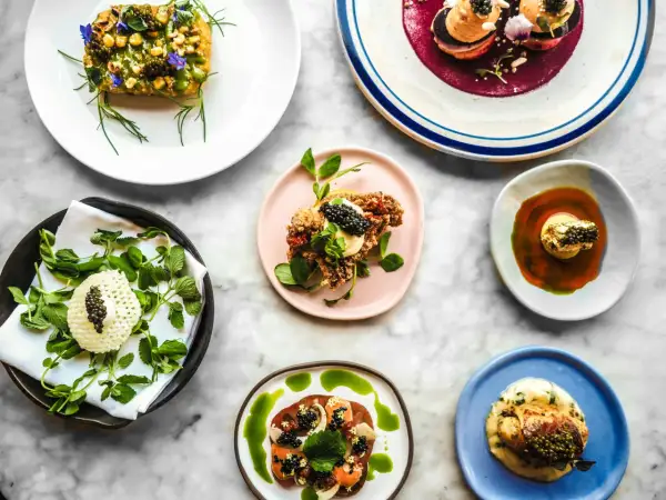 Deliciosos platos de un menú degustación, con caviar, flores comestibles y salsas vibrantes, presentados sobre una mesa de mármol.