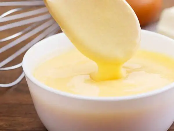 Crema pastelera cremosa cayendo de una cuchara a un bol. ¡Es bueno saber que se puede congelar la crema pastelera para usarla más tarde!