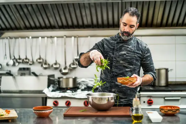 Chef con barba añade hierbas a un bol. Su trabajo en la direccion de cocina FP es impecable.