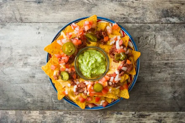 Nachos con queso derretido, carne, tomate, cebolla y jalapeños, con guacamole en el centro.