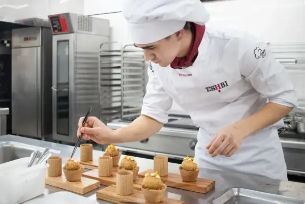 Joven chef perfecciona pequeños bocados, demostrando su dominio en ciencias culinarias y gastronómicas.