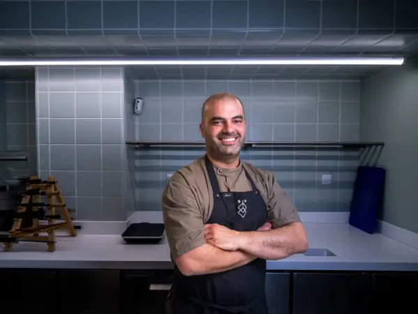 Chef sonriente con delantal negro en una cocina moderna, uno de los cocineros vascos famosos.