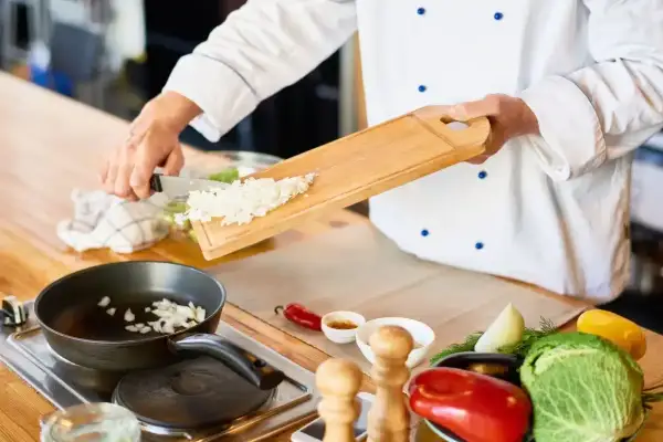 Un jefe de cocina, con su blanco uniforme, prepara cebolla picada para una sartén. Un convenio de sabor se inicia.