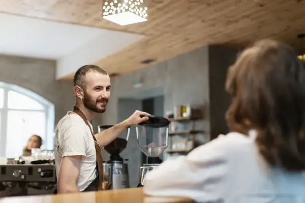 Barista sonríe mientras prepara café, un paso más para abrir su restaurante.