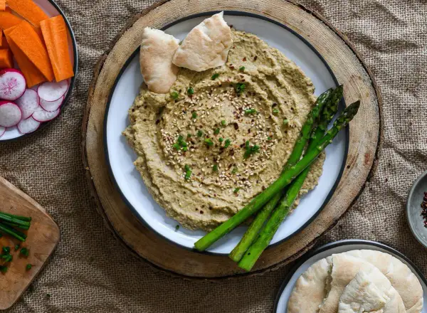 Hummus cremoso con espárragos, pan de pita y crudités de zanahoria y rábano. ¡Perfecto para tus ideas de picoteo saludables!