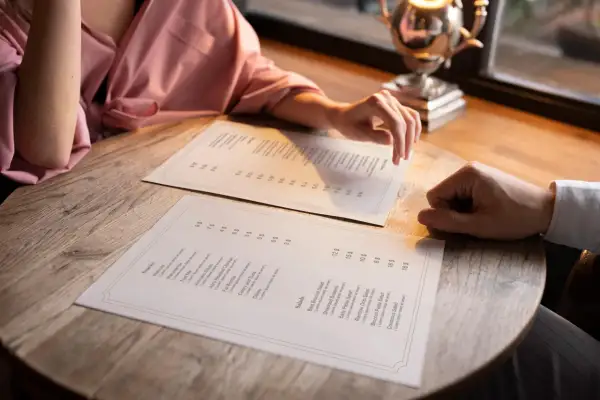 Pareja revisa el menú para decidir cómo hacer una carta de restaurante. Se ven platos como ensaladas y snacks.