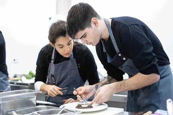 Dos aprendices de cocina, concentrados en emplatar un plato, aprendiendo como ser chef.