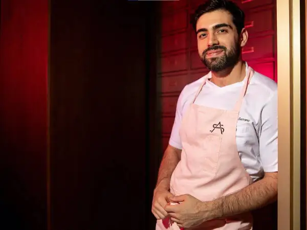 Chef Serrano, parte de la lista cocineros estrellas Michelin, sonríe con delantal rosa.