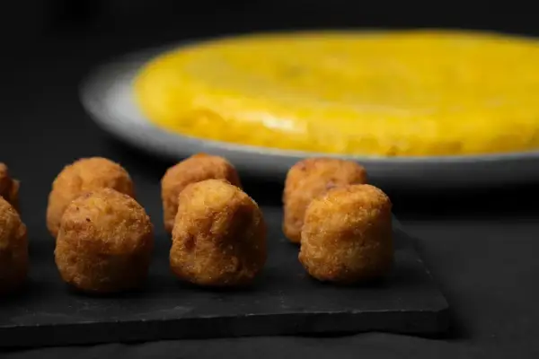 Croquetas doradas y crujientes, un ejemplo de que es la quinta gama hostelería, con una tortilla española al fondo.