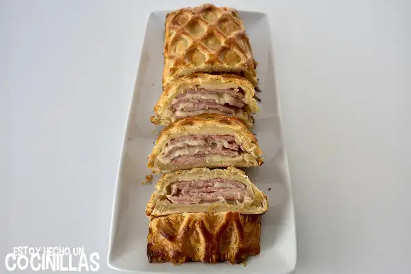 Delicioso hojaldre jamón york y queso al horno, cortado en porciones, con una capa crujiente y relleno jugoso.