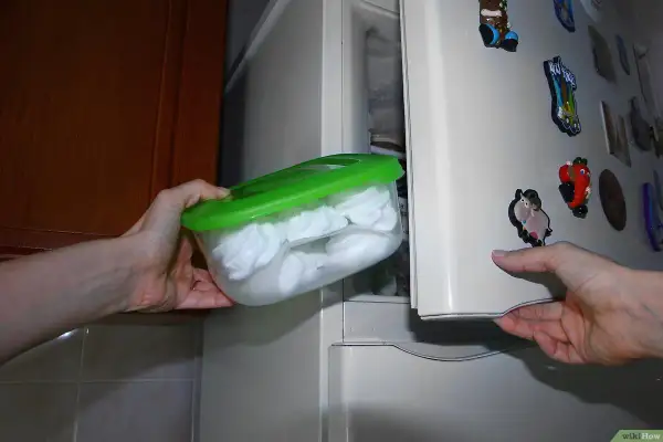 Manos guardan un recipiente con merengues blancos en el congelador. Así se puede congelar el merengue para conservarlo.